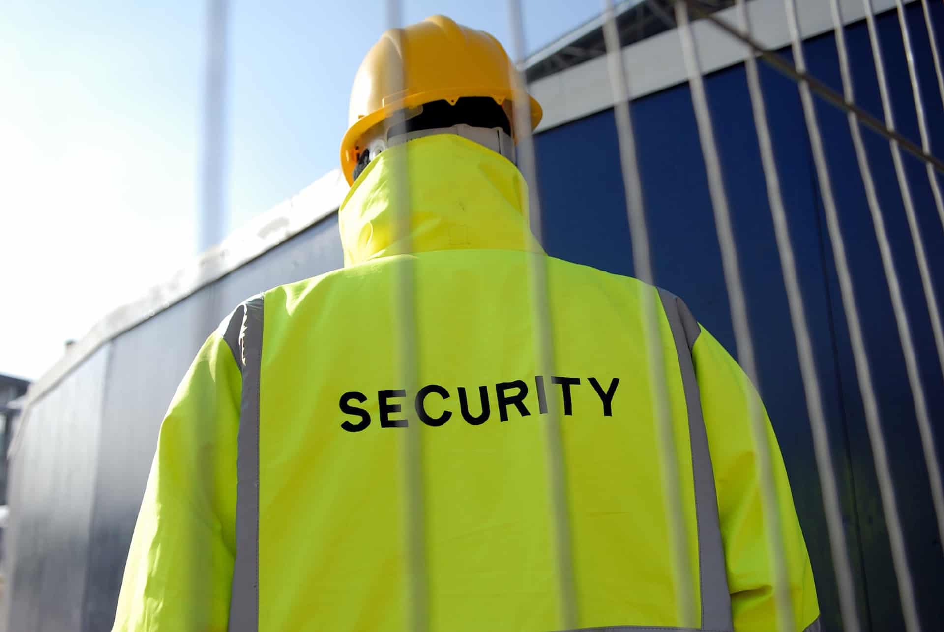 Industrial security guard in high visibility jacket behind a fence